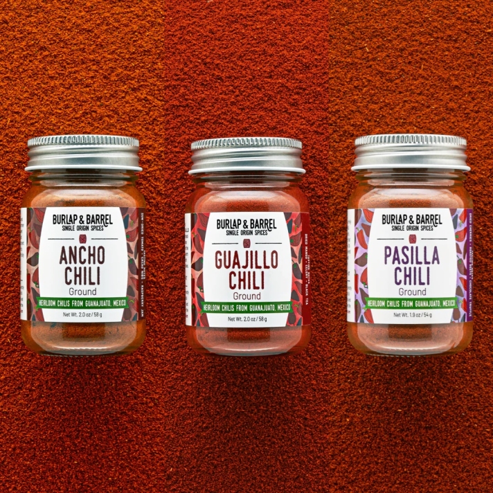Trio of Mexican chili powders — ancho, guajillo, and pasilla — on red background